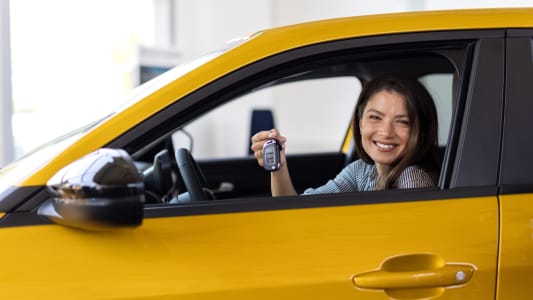 Femme souriante tenant des clés dans une voiture jaune.