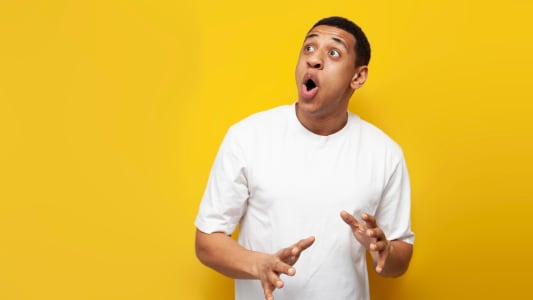 jeune homme afro-américain choqué en t-shirt blanc surdimensionné est surpris sur fond jaune isolé