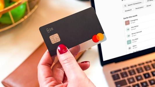 Main tenant une carte bancaire devant un ordinateur portable.