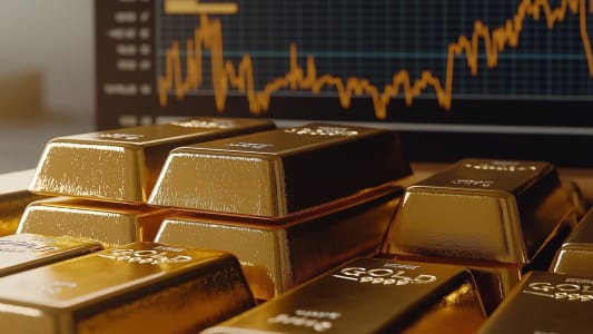 Lingots d'or devant un cran affichant des graphiques financiers.