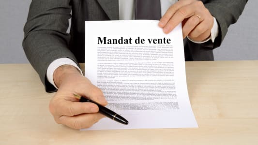 Homme en costume prsentant un document intitul Mandat de vente.