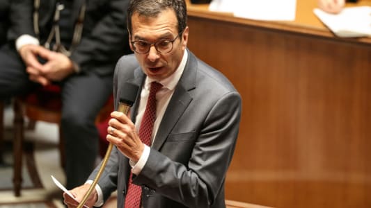 Homme en costume parlant au micro dans une salle formelle. Farandou