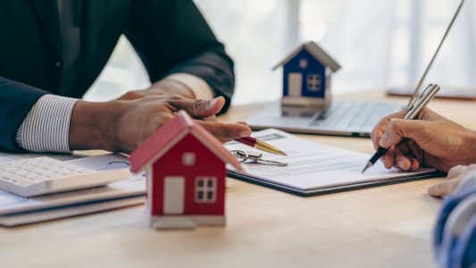 Signature de documents immobiliers avec des maisons miniatures.