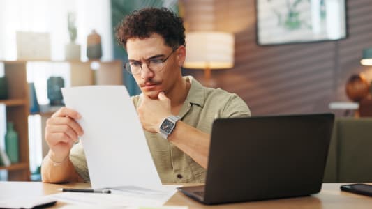 Un homme regarde un document devant son ordinateur.