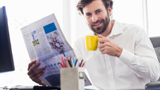 Homme souriant lisant un journal avec tasse de caf�.