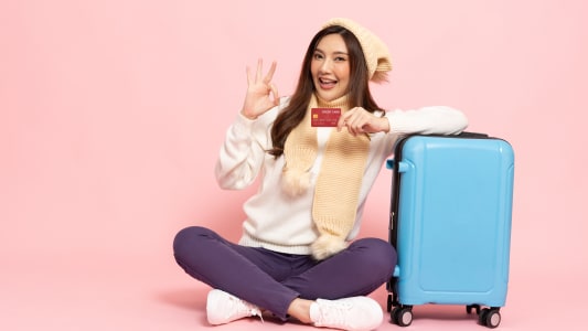 Une femme souriante à côté d'une valise avec une carte bancaire.
