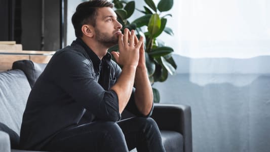 vue de côté d'un bel homme pensif assis sur le canapé et regardant