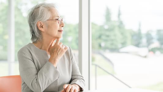 Femme âgée réfléchit près de la fenêtre lumineuse.