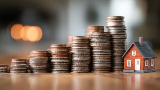 Piles de pices avec petite maison rouge sur table.