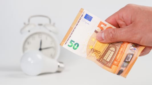 Billet de banque en euros en main avec ampoule et rveil flou en arrire-plan