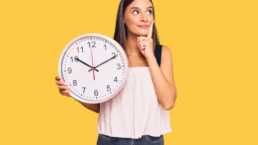 Une jeune femme tenant une grande horloge avec un visage s�rieux.