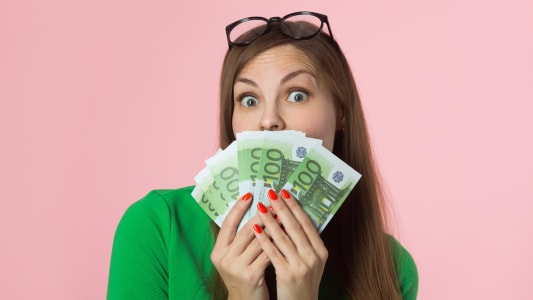 Une femme tenant des billets de 100 euros et sur un fond rose avec un visage surpris