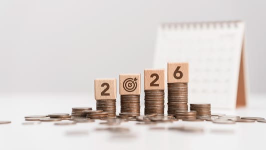 Des piles de pièces avec un calendrier et des blocs de bois formant le numéro 2026.