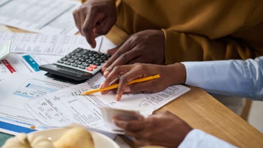 Gros plan sur les mains de deux personnes calculant ensemble leurs imp�ts � l'aide d'une calculatrice et regardan des documents financiers � table.