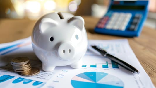 Tirelire avec pi�ces, calculatrice et documents financiers sur table.