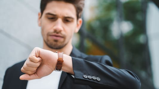 Homme d'affaires ou étudiant regarde sa montre. Jeune homme pressé en retard pour le travail. Mannequin masculin sur fond de bâtiment de bureau.