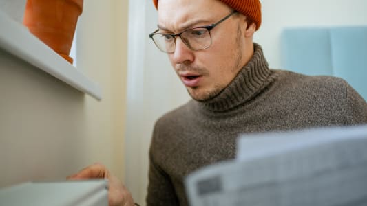 Jeune homme portant un bonnet ajustant le thermostat sur un radiateur.