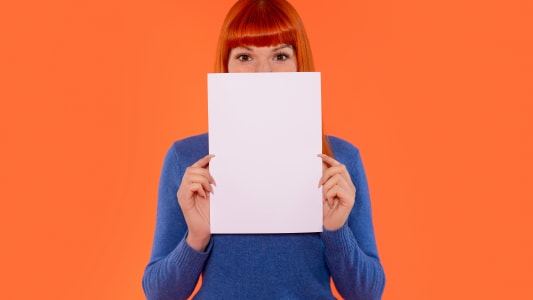 Jeune femme en pull bleu tenant une feuille de papier vierge devant son visage contre un fond orange vif lors d'une s�ance photo cr�ative