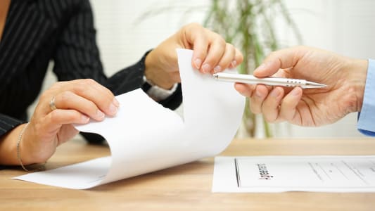 Quelqu'un d�chire des documents devant une autre personne qui tend un crayon pour signer.