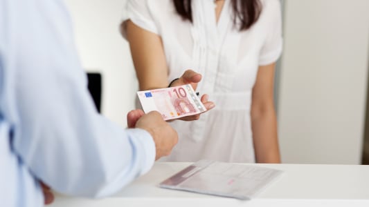 Une personne tendant un billet � une autre personne en blouse blanche.