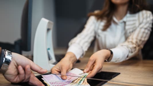 Une femme d'affaires travaille dans un bureau de change. Elle donne de l'argent liquide &agrave; un client.