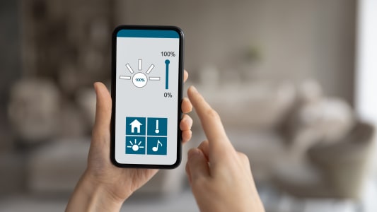 Gros plan sur une personne tenant un t&eacute;l&eacute;phone avec une application de maison intelligente sur l'&eacute;cran.