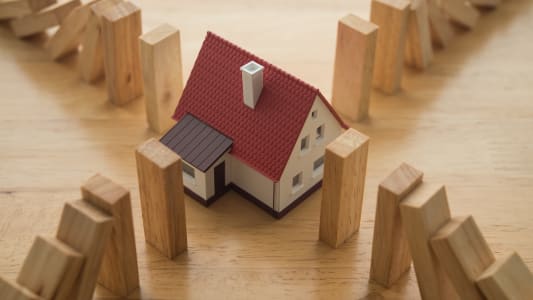 Maison entour&eacute;e de blocs de bois tombant comme des dominos.