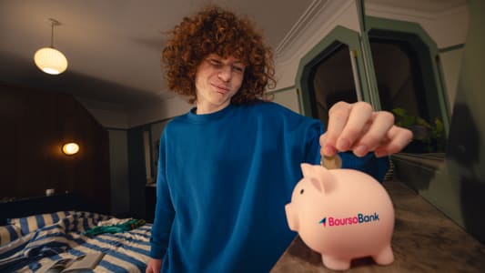 Un jeune met une pi&egrave;ce dans une tirelire Boursobank.