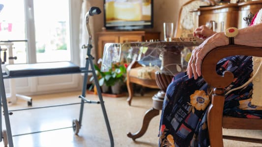 Personne &acirc;g&eacute;e &agrave; domicile avec d&eacute;ambulateur et t&eacute;l&eacute; alarme regarde la t&eacute;l&eacute;vision