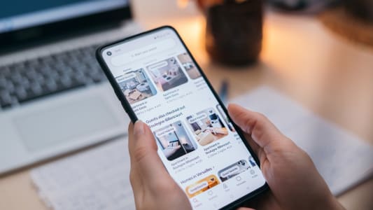 Personne cherchant un logement sur une application mobile, ordinateur derrière.