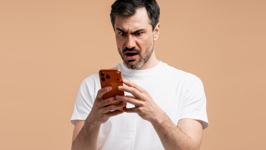 Un homme l'air surpris en regardant son t&eacute;l&eacute;phone.