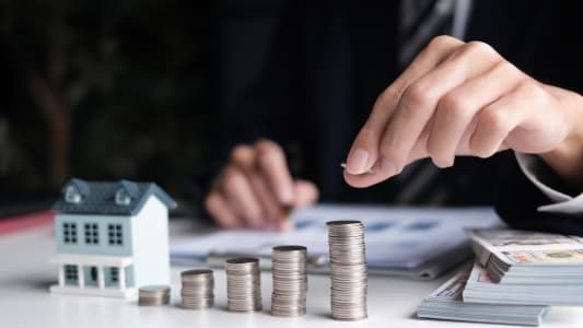 Une maison miniature et des piles de pi&egrave;ces de monnaie.