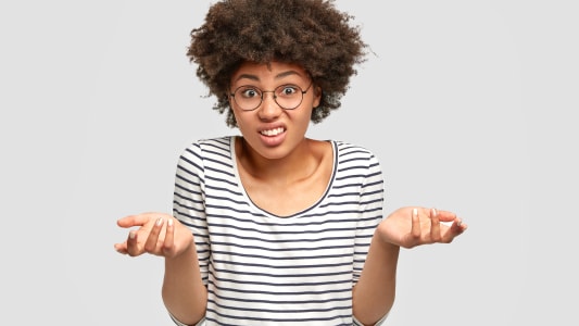 Mod&egrave;le f&eacute;minine afro-am&eacute;ricaine h&eacute;sitante en studio, ayant une expression perplexe, hausse les &eacute;paules avec incertitude, fron&ccedil;ant les sourcils. Femme cliente douteuse ne peut pas faire de choix, isol&eacute;e sur un mur blanc.
