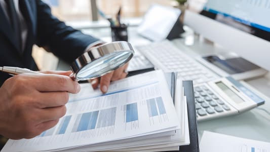 Homme examine des documents financiers avec une loupe au bureau.