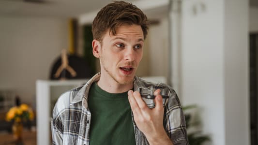 Jeune homme enregistrant un message vocal sur un smartphone à l'intérieur