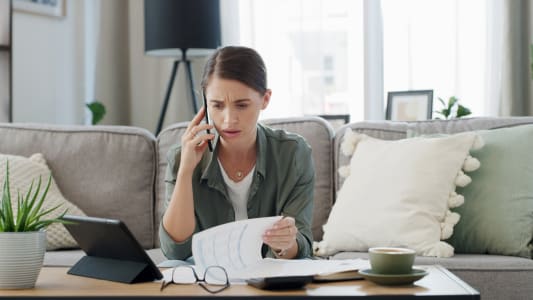 Une femme regarde des documents avec t&eacute;l&eacute;phone &agrave; l'oreille.