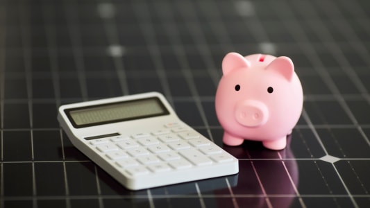 Gros plan d'une calculatrice blanche et d'une tirelire rose sur un panneau solaire photovolta&iuml;que.