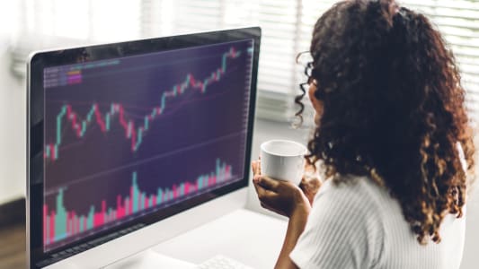 R&eacute;ussite d'une jeune femme d'affaires afro-am&eacute;ricaine, trader, qui &eacute;change des graphiques de march&eacute; boursier, vend et ach&egrave;te avec des graphiques financiers et des donn&eacute;es sur son ordinateur de bureau &agrave; la maison.