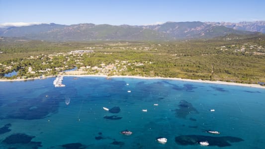 Plage de sable, mer turquoise, bateaux, for&ecirc;t, montagnes en arri&egrave;re-plan.