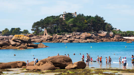 Brittany, France. Des personnes non reconnaissables se baignent et se détendent sur la plage avec une vue sur le château de la Côte de Granit Rose près de Ploumanach. Vacances en famille sur fond de Côtes d'Armor.
