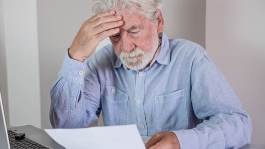 Un vieil homme paraissant stress&eacute; en lisant des documents &agrave; son bureau.