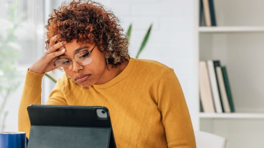 Une femme stressée devant une tablette et des documents.