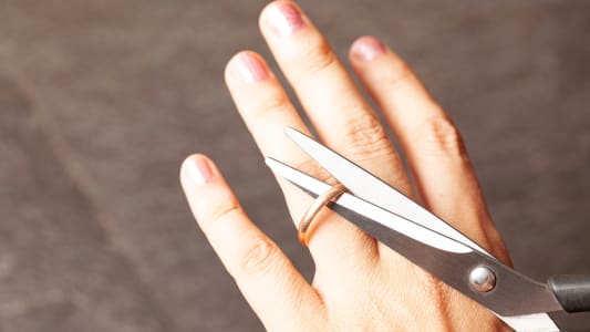 la main d'une femme coupe une bague de fian&ccedil;ailles avec des ciseaux
