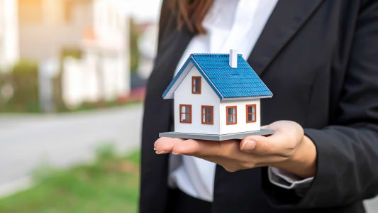 Une main tient une petite maison miniature, fond flou.