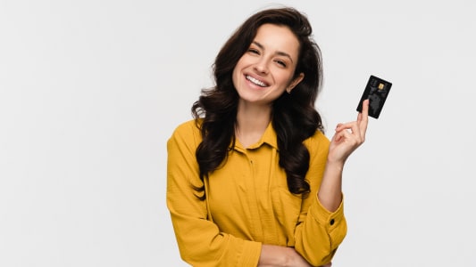 Belle jeune fille étudiante hispanique latine tenant et présentant une carte bancaire de crédit pour un paiement en ligne isolé sur fond blanc. Concept de technologie bancaire de magasinage en ligne