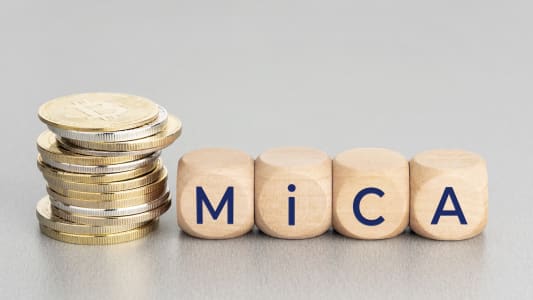 Pièces de monnaie Bitcoin et cubes écrivant MICA sur table.