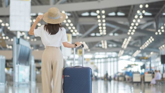 Une jeune femme tenant la poignée de sa valise et vérifiant l'heure de son voldans un aéroport.