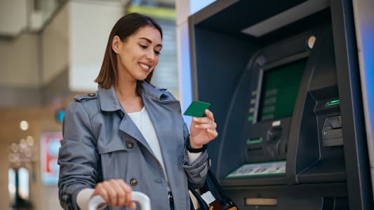 Voyageuse heureuse utilisant sa carte de crédit au distributeur automatique à l'aéroport.