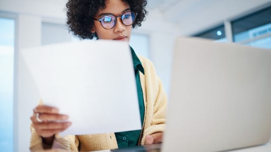 Une femme devant un ordinateur portable tenant des documents.