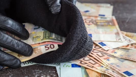 Des mains dans des gants de cuir noir mettant des billets dans un sac.
